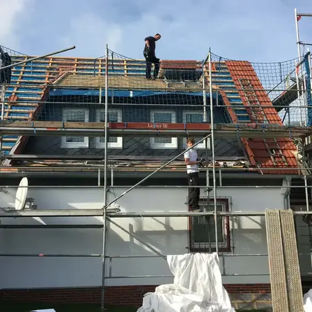 Arbeiter führen Dachsanierung mit Gerüst und Sicherheitsnetz an einem Wohnhaus durch.