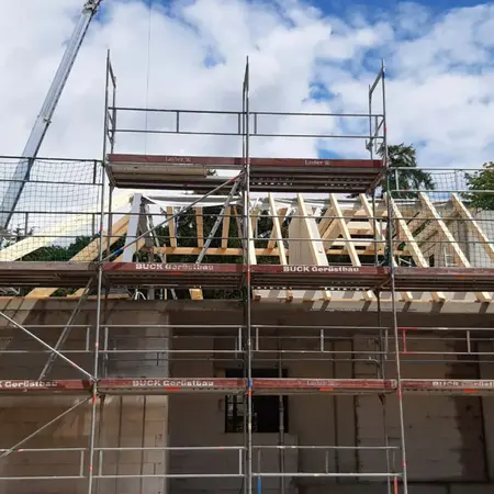 Hausbau mit Holz-Dachkonstruktion und Baugerüst unter blauem Himmel auf Baustelle.