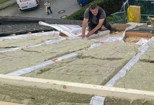 Ein Handwerker verlegt Dämmmaterial auf einem Hausdach zur energetischen Sanierung.