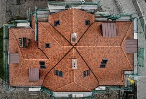 Dach eines Hauses mit roten Dachziegeln, mehreren Fenstern und Schornsteinen aus der Vogelperspektive.