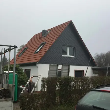 Einfamilienhaus mit rotem Satteldach, Schieferfassade und Dachfenstern im Nebel.